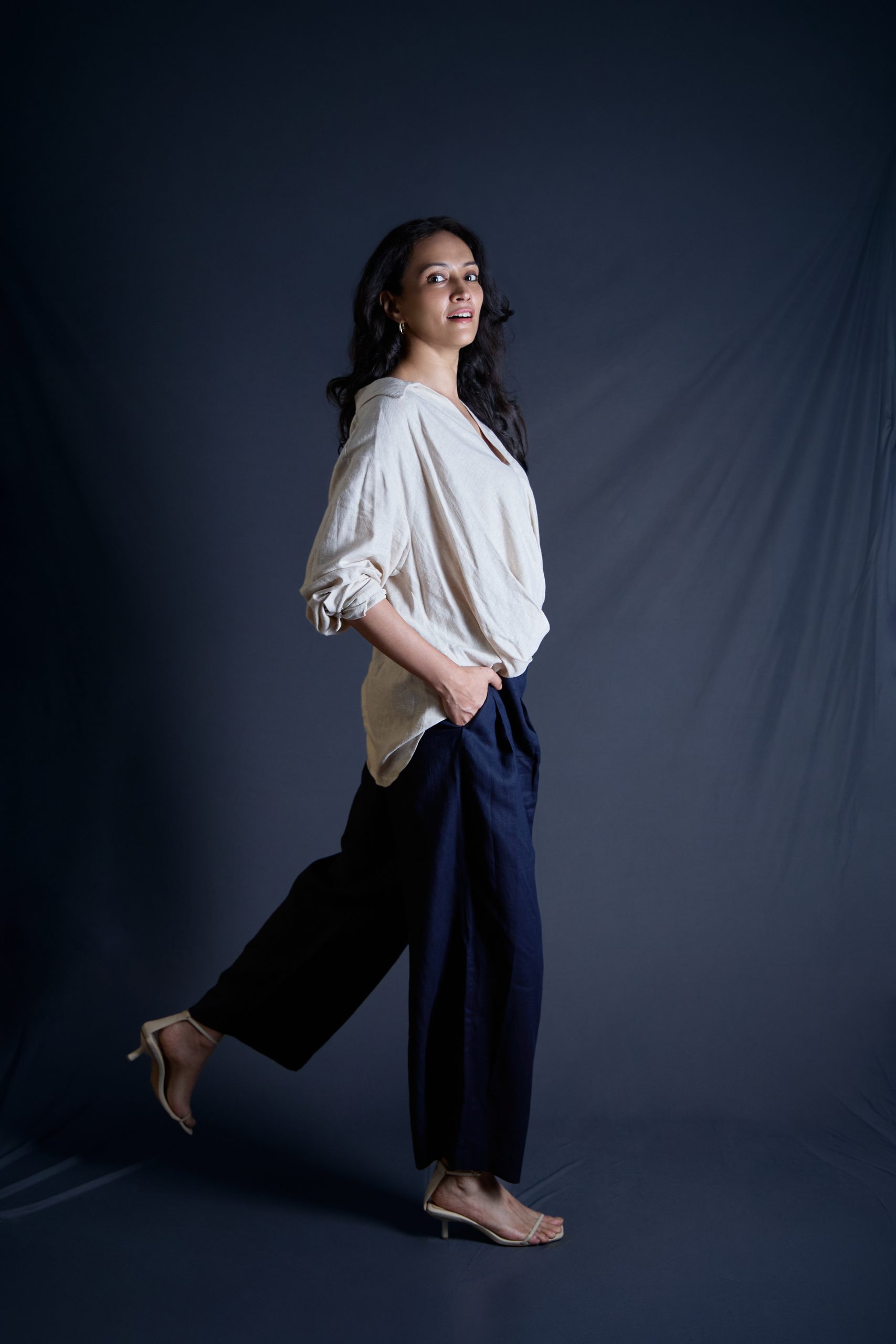 Model mid-stride in a white shirt and wide black trousers on a navy backdrop